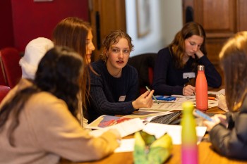 a group of young students sat at a table talking with papers spread across the table